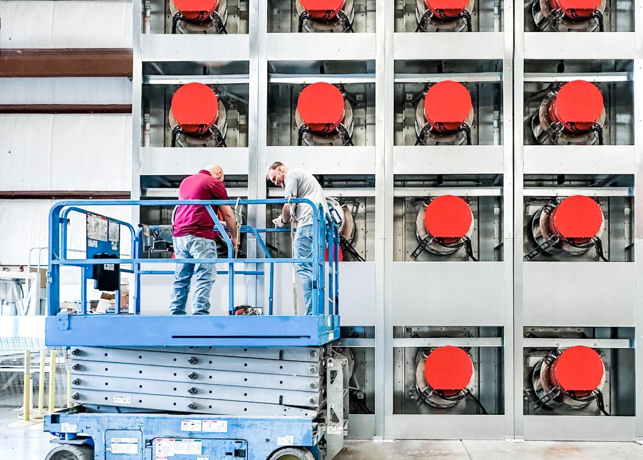 Some workers stand on a hydraulic lift in front of a data center.