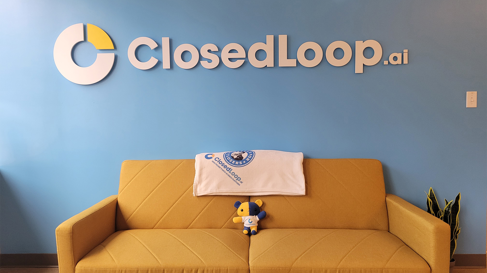 A yellow couch against a blue wall featuring ClosedLoop’s logo. 