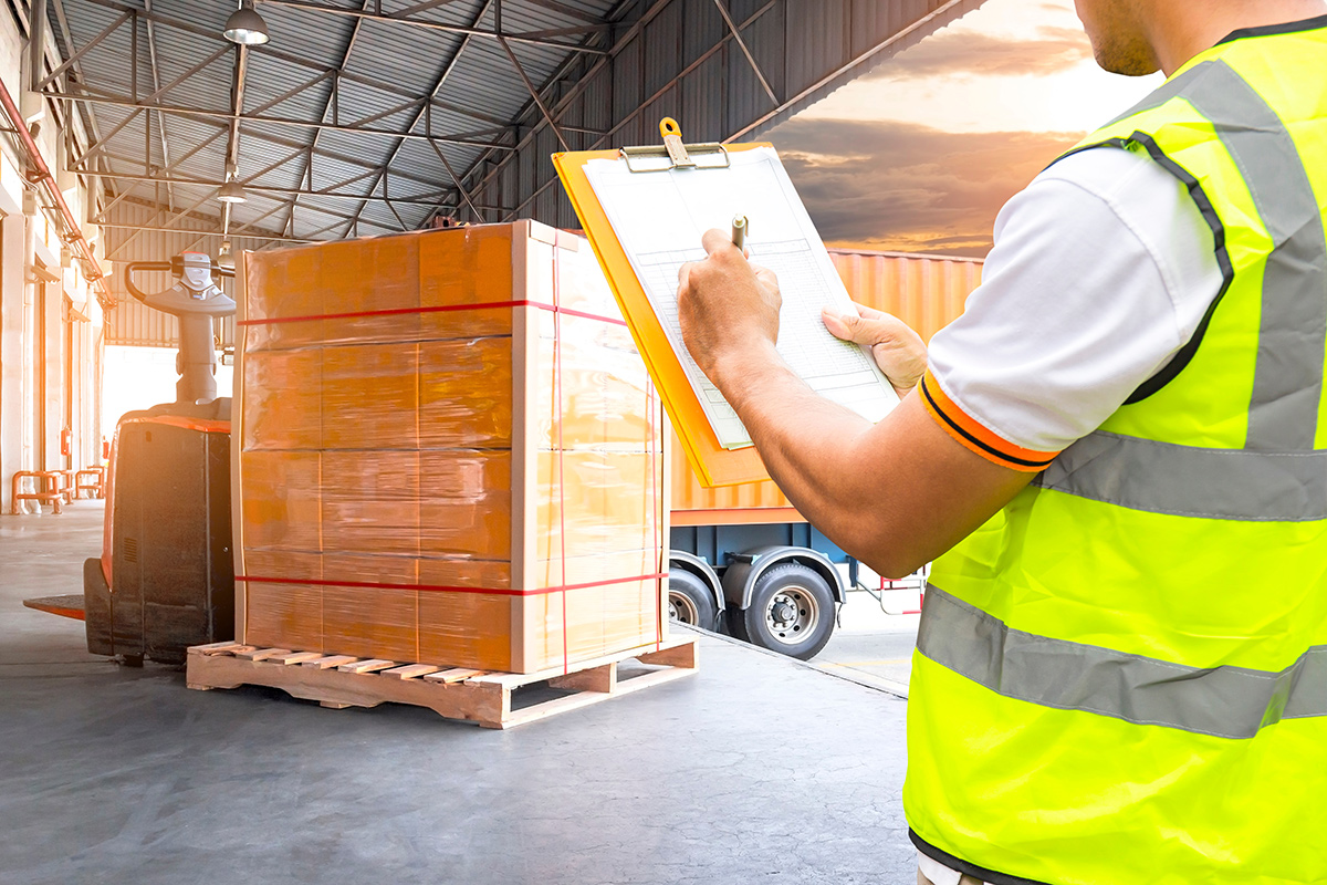 Worker holding clipboard inspecting document in a shipping warehouse