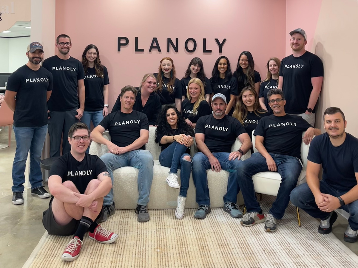 Planoly team photo in front of a pink wall with the company logo on it