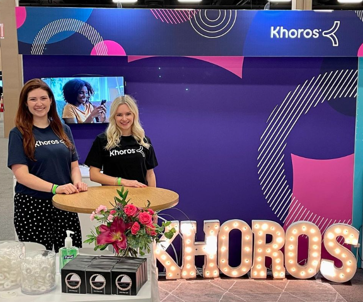 two Khoros employees standing in front of lit up Khoros sign