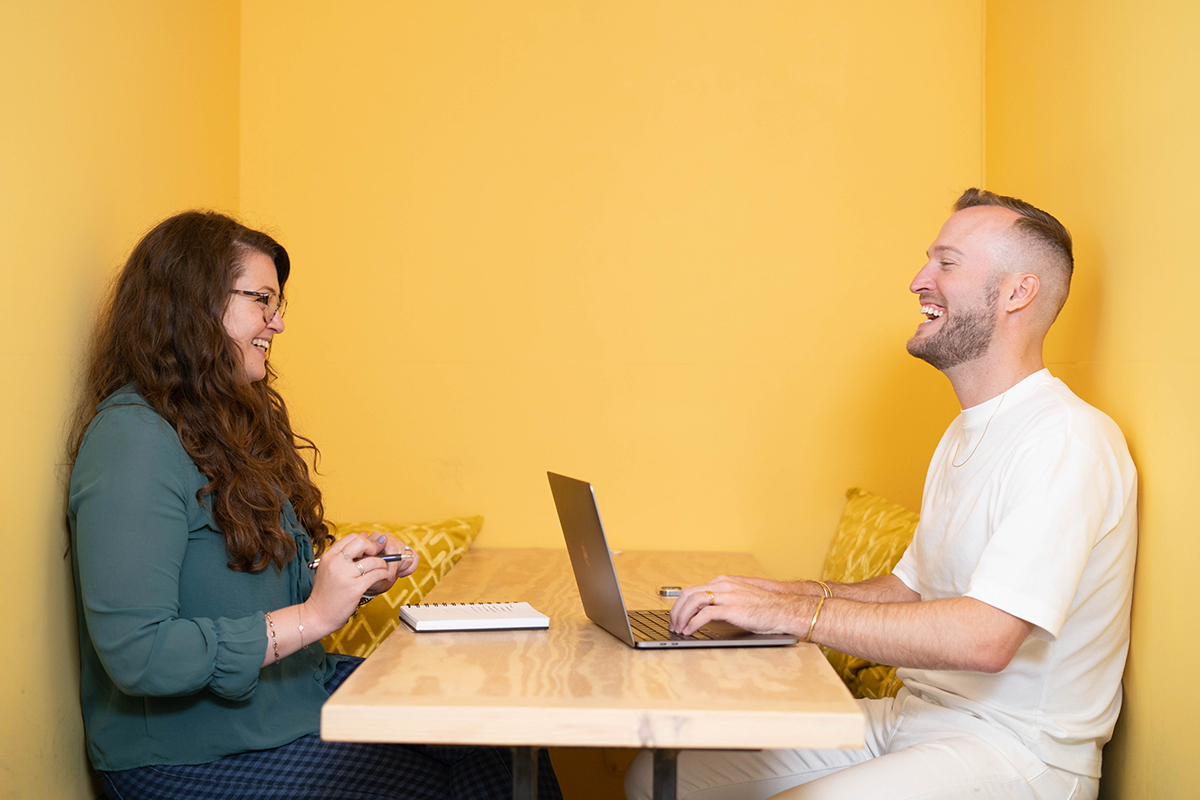 Yotpo coworkers having a meeting sitting across from each other in a booth with yellow walls 