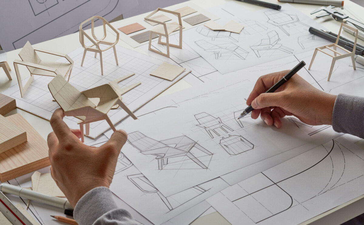 A designer sketches a chair and looks at miniature 3d prototypes. 