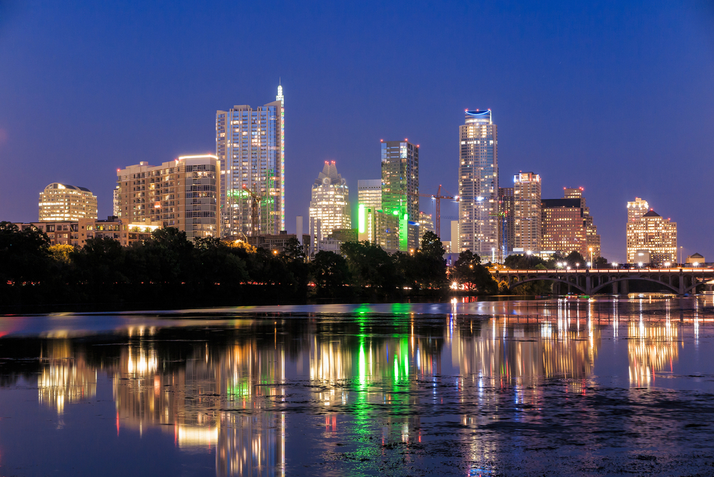 Downtown Austin, Texas at night with lights from skyscrapers reflecting on the near lake.