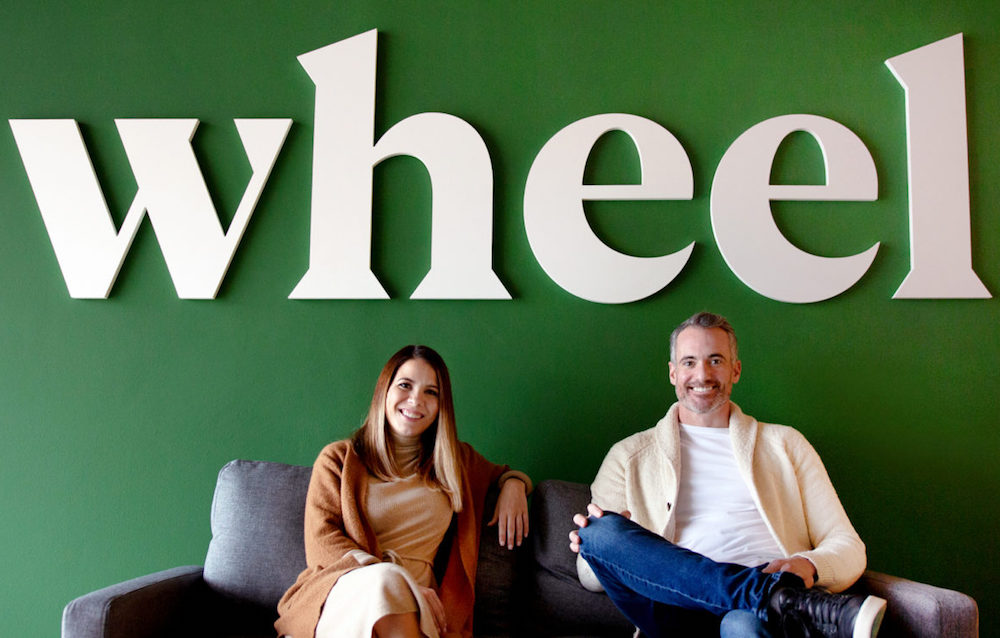 The two Wheel co-founders sitting on a couch in front of their company logo.