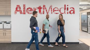 AlertMedia team members walking past company logo on the wall in the office