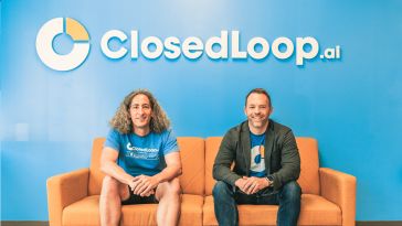 Closedloop team members sitting on a couch with the Closedloop logo on the wall behind them
