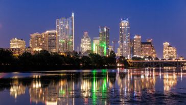 Downtown Austin, Texas at night with lights from skyscrapers reflecting on the near lake. 