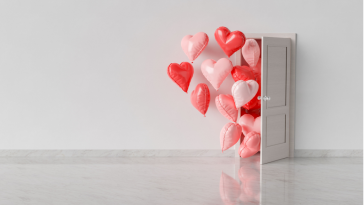 Red, pink and white heart balloons coming out of a white door into a white room