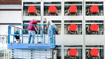 Some workers stand on a hydraulic lift in front of a data center..