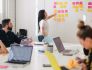Team meeting with woman standing at wall looking at colorful sticky notes
